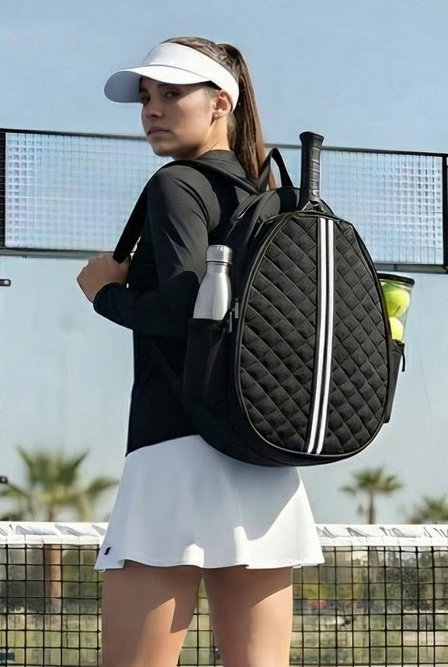 A female padel player on a court wearing a black long-sleeve top and white skirt, carrying the premium black quilted SVL padel backpack.