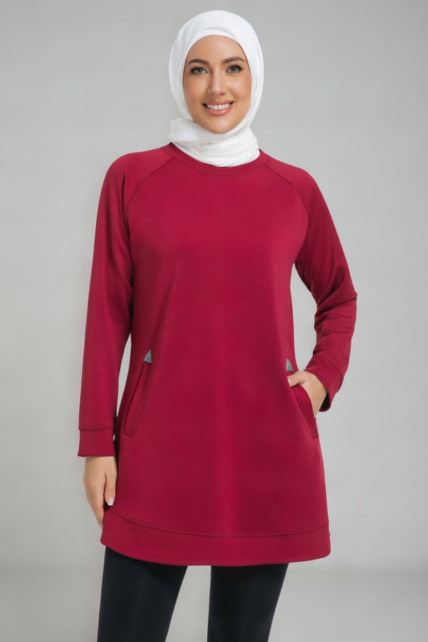 A female player wearing a modest maroon SVL padel tunic with long sleeves, side pockets, and a white hijab, designed for comfort and performance on the court.