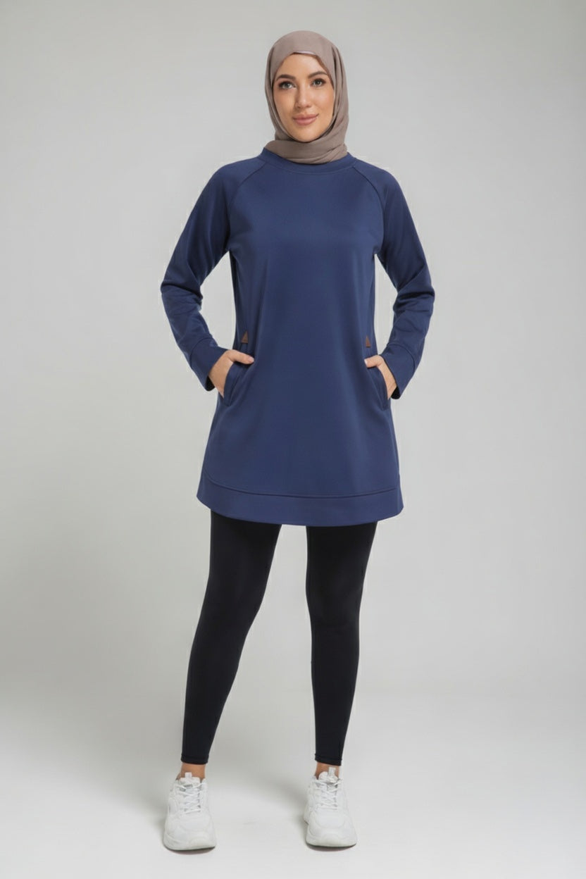 Full-length studio view of a female player wearing a modest navy blue SVL padel tunic, black leggings, and white sneakers, styled with a taupe hijab.