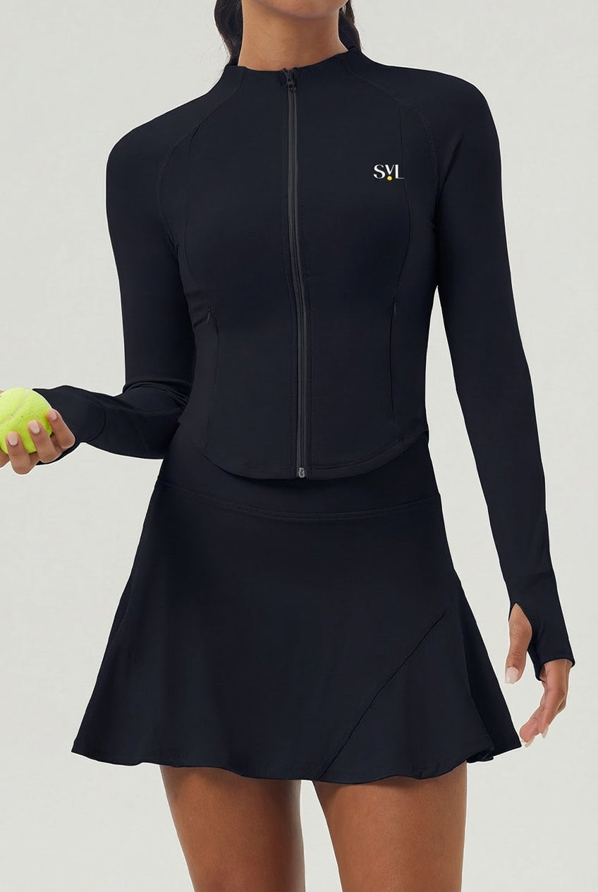 A woman wearing the black Swan Sway performance jacket with a matching athletic skirt, designed for tennis and padel matches.