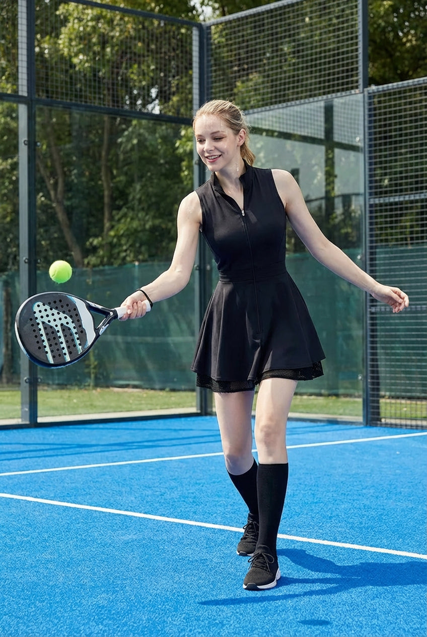 A female padel player on a blue court wearing the black Wiktoria padel dress, designed with a breathable mesh-lined flared skirt for tennis and padel.