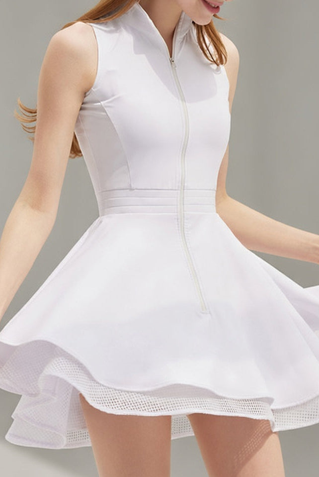 A female athlete in a white Wiktoria performance tennis and padel dress featuring a sleeveless zip-up bodice and a double-layered flared skirt with mesh trim.