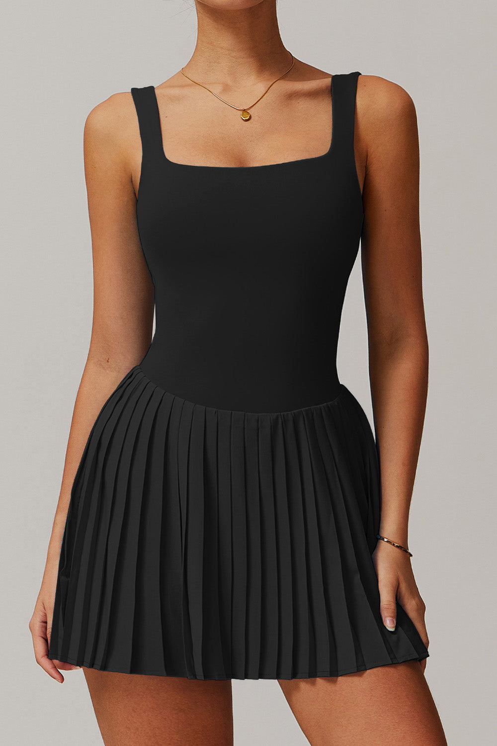 Front studio shot of the black Daria performance tennis and padel dress with a modern square neck and pleated athletic skirt.