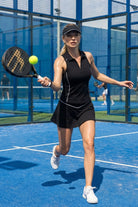 A female padel player in motion on a blue court wearing the black SVL Kate skirt and matching sleeveless polo top.