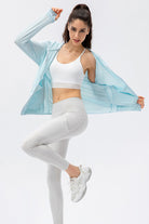 A woman wearing the light blue SVL Maya Jacket over a white sports bra and leggings, demonstrating the jacket's lightweight and flexible movement.