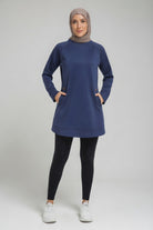 Full-length studio view of a female player wearing a modest navy blue SVL padel tunic, black leggings, and white sneakers, styled with a taupe hijab.