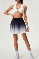 Full-length studio shot of the black ombre Valeria pleated skirt paired with a white performance sports bra and sneakers.