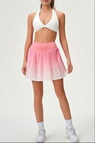 Full-length studio shot of the pink ombre Valeria pleated skirt paired with a white sports bra and sneakers, ideal for tennis and padel.