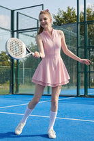 A female padel player on a blue padel court holding a racket, wearing the pink Wiktoria athletic dress with white performance socks.