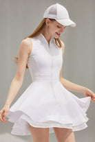 A female athlete in a white Wiktoria performance tennis and padel dress featuring a sleeveless zip-up bodice and a double-layered flared skirt with mesh trim.