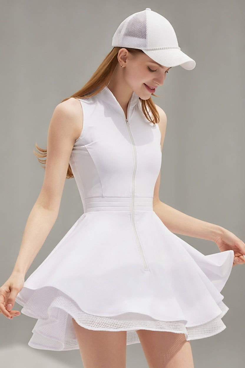 A female athlete in a white Wiktoria performance tennis and padel dress featuring a sleeveless zip-up bodice and a double-layered flared skirt with mesh trim.