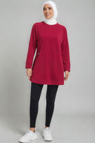 Full-length view of a female player in a maroon SVL modest padel tunic, black leggings, and white sneakers, featuring a white hijab.